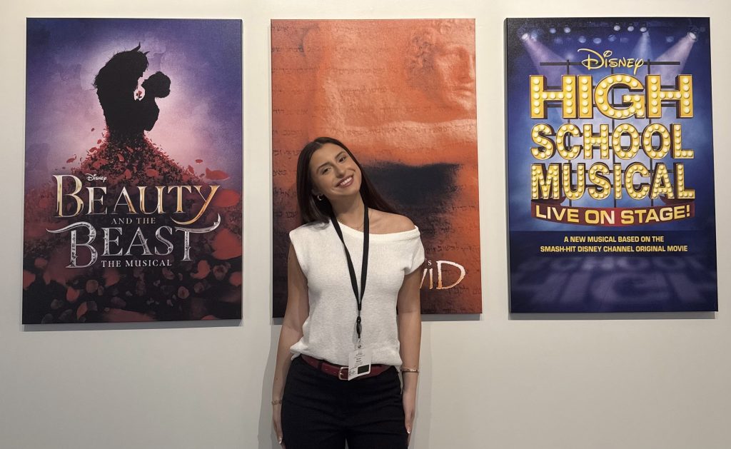 The author stands in front of a wall of three posters in the office of the Disney Theatrical Group above New York's New Amsterdam Theater.