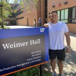 Luis Rodrigues stands next to the blue and black sign for Weimer Hall