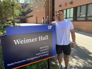 Luis Rodrigues stands next to the blue and black sign for Weimer Hall