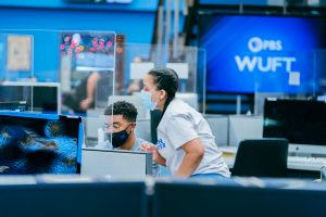 Two students lean over a computer in the Innovation News Center. newsroom