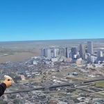 A woman wearing a VR headset with the view from inside the headset, a city skyline, visible behind her.