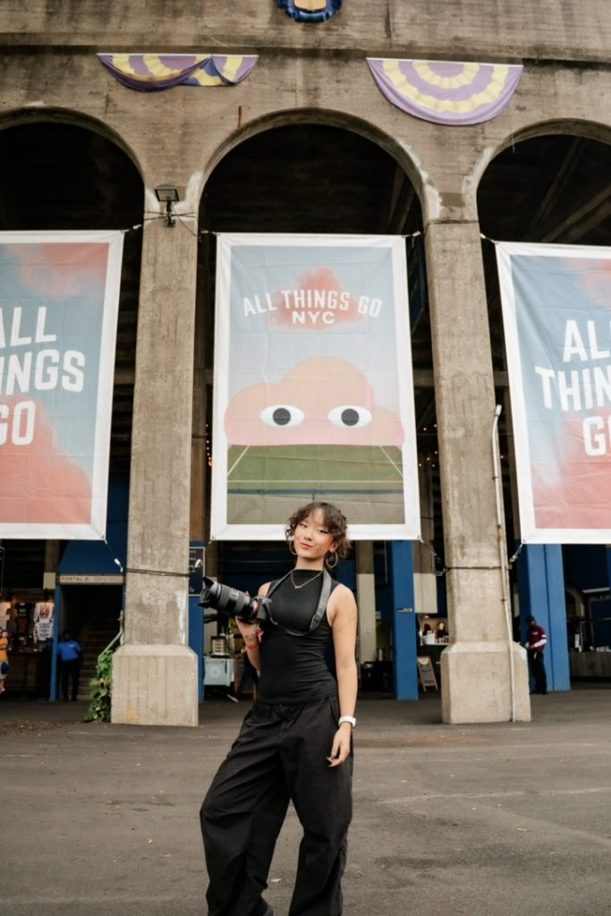 Tiffany Fang with camera standing in front of "All Things Go" festival signs.