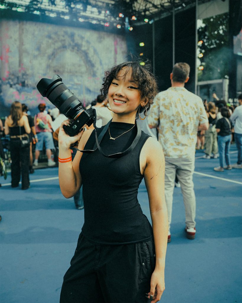 Tiffany Fang holding a camera and an outdoor venue at a festival. 