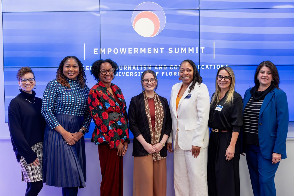 A group of women stand in front of a sign at a conference.