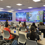 Students from the Atlas Lab and the Motor Bella F1 club react in shock while watching an F1 car crash on the Atlas Lab screens.