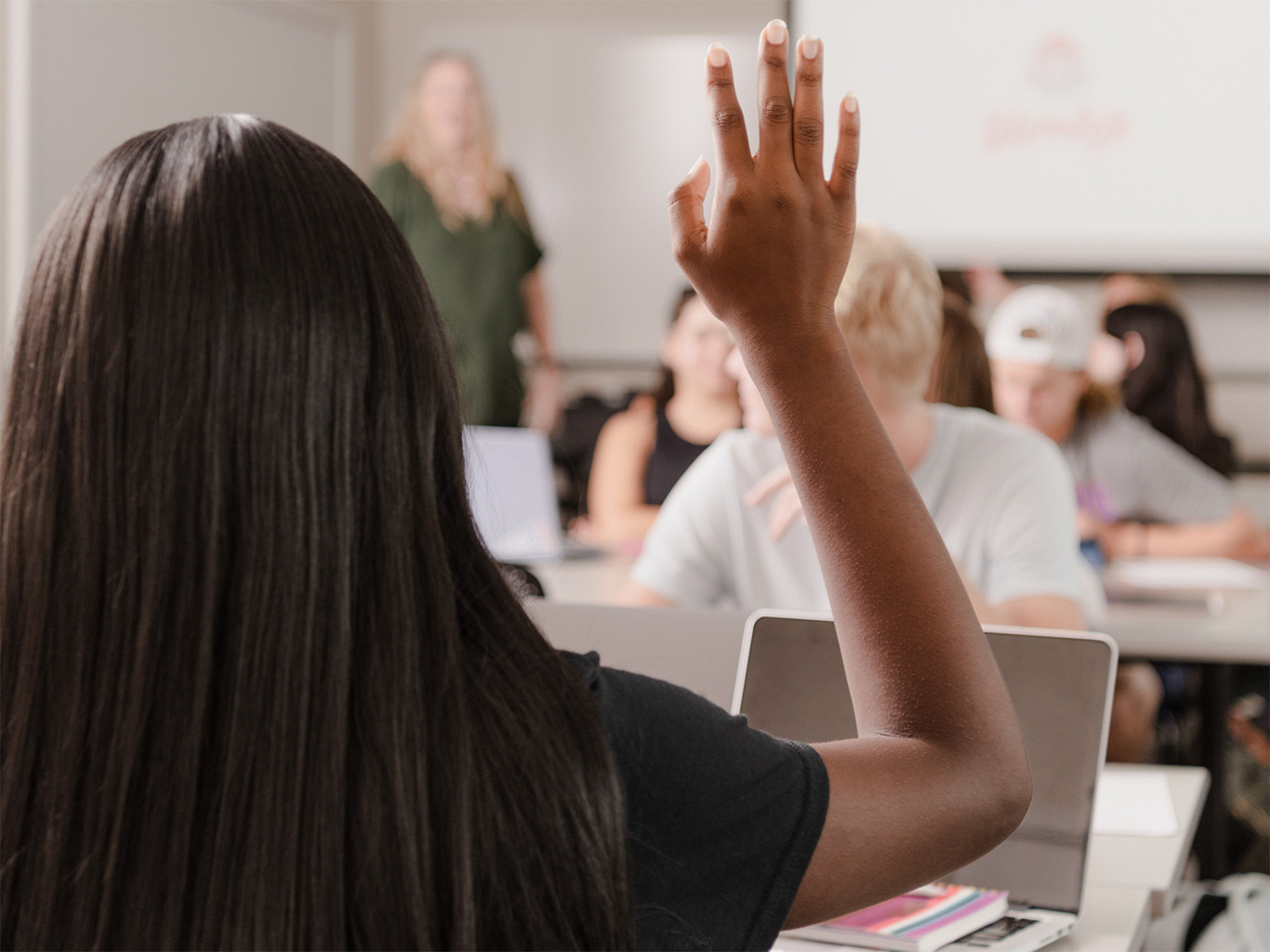 A person raises a hand in a classroom.