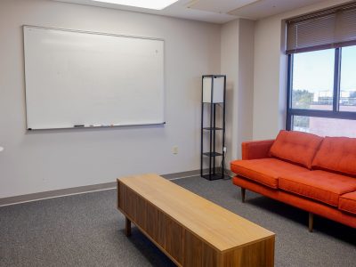 Casual meeting room with orange couch in front of window and dry-erase board on adjacent wall.