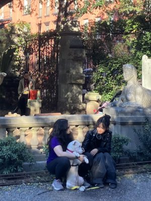 A pair of woman with a white dog seated in a garden.