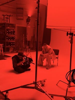 A photographer and subject in a photo studio. The photo is tinted red overall.